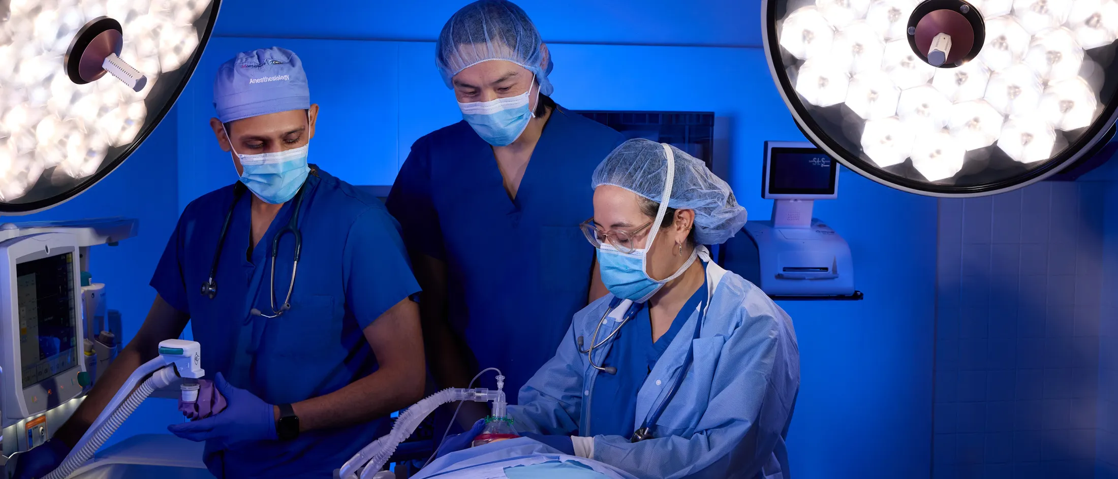 Three medical professionals in scrubs and masks performing a procedure in a brightly lit operating room