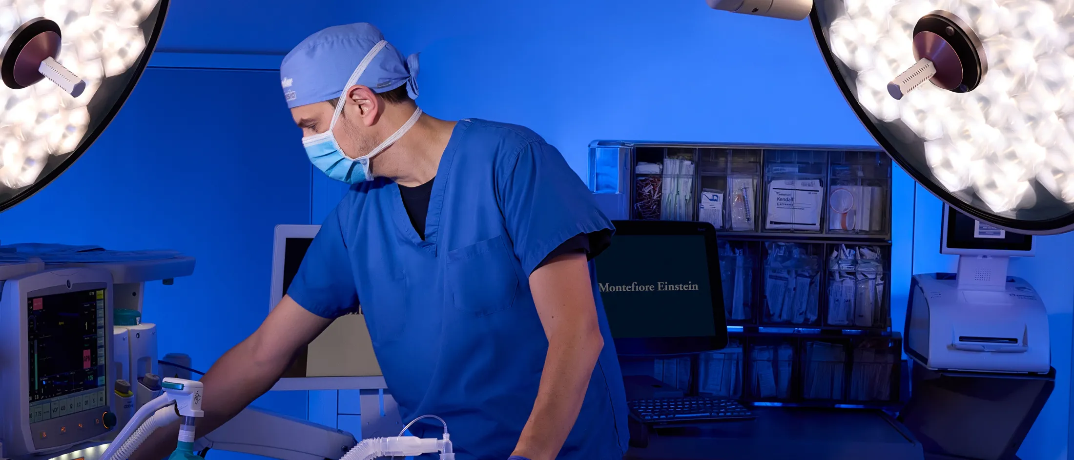 Anesthesiologist adjusting equipment in a blue-lit operating room