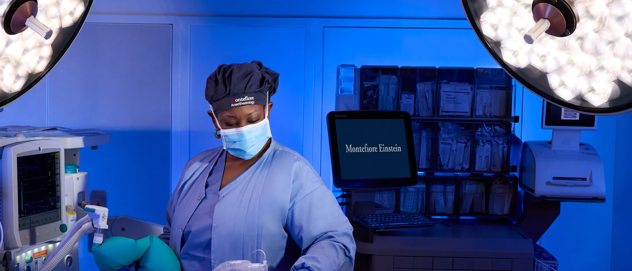 Anesthesiologist in surgical attire monitoring a patient in the operating room with medical equipment in the background.