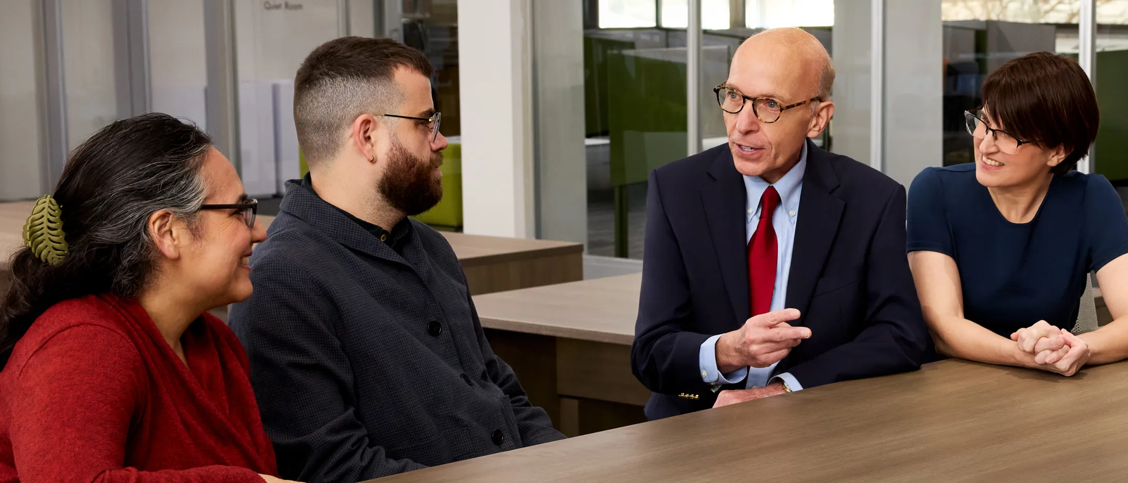 Four colleagues having a discussion around a wooden table in a modern office space