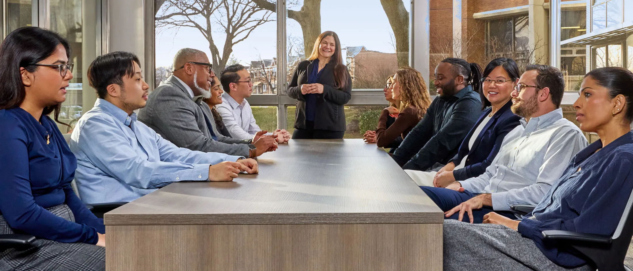 Team seated around a large conference table with one person standing and smiling during a meeting