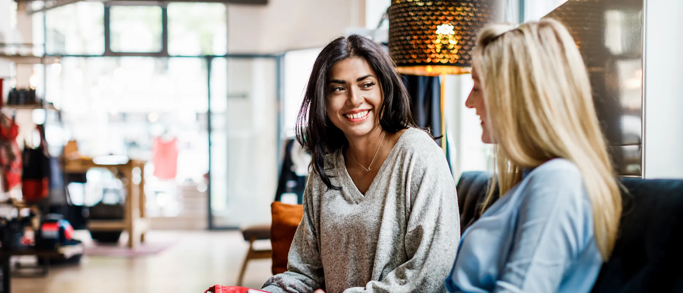 Smiling woman chatting with a friend on a sofa in a bright modern café.