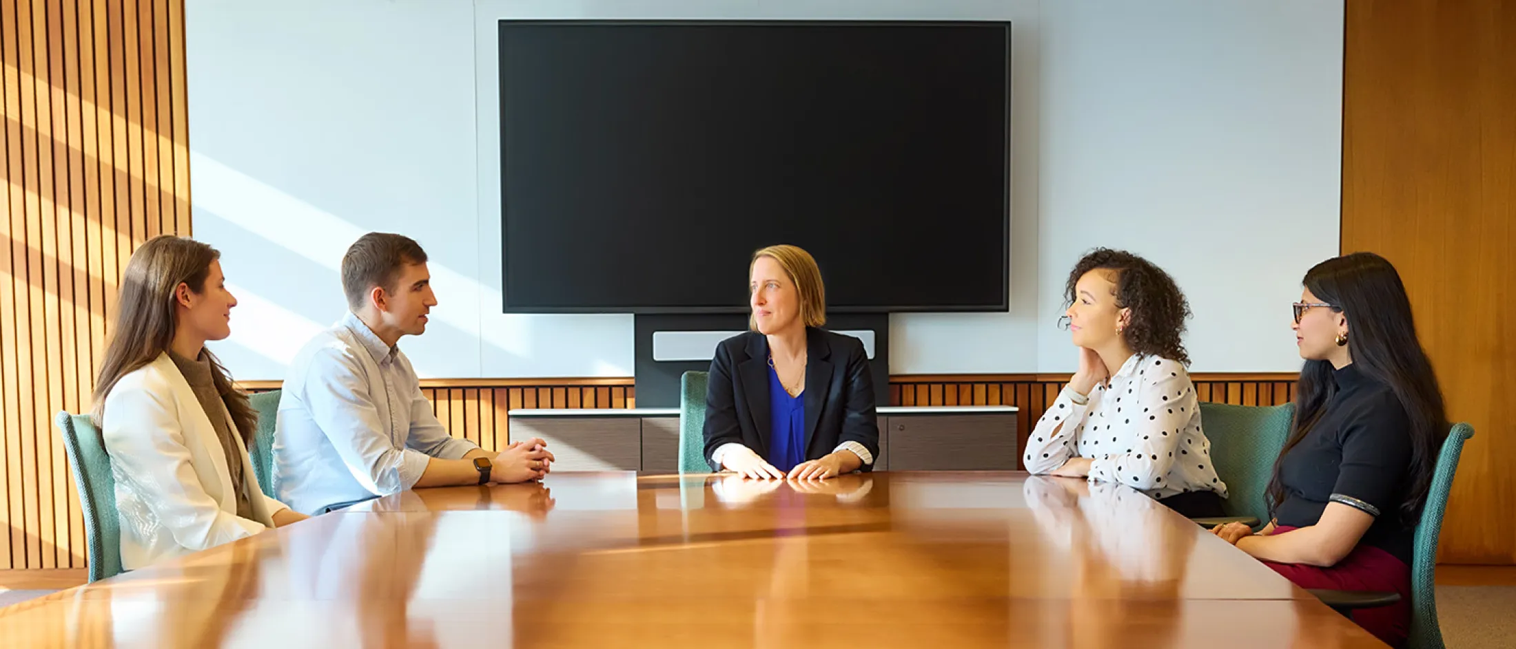 Group of five people seated around a boardroom table having a professional meeting