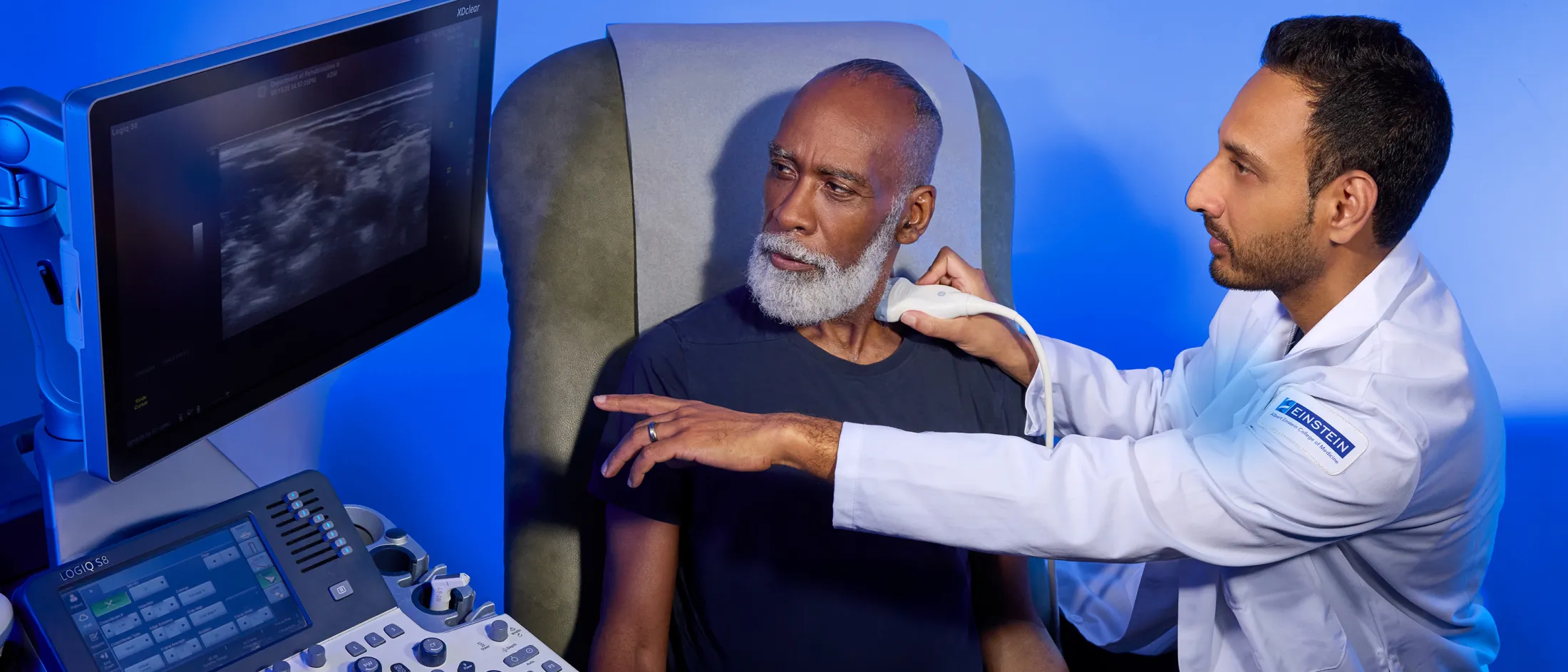 Doctor performing an ultrasound on an older man's neck while both look at the screen.
