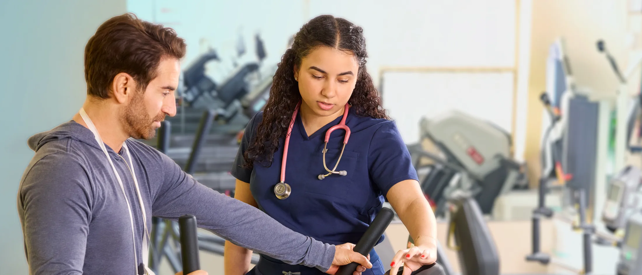 Nurse assisting a man on an exercise machine during a rehabilitation session in a gym.