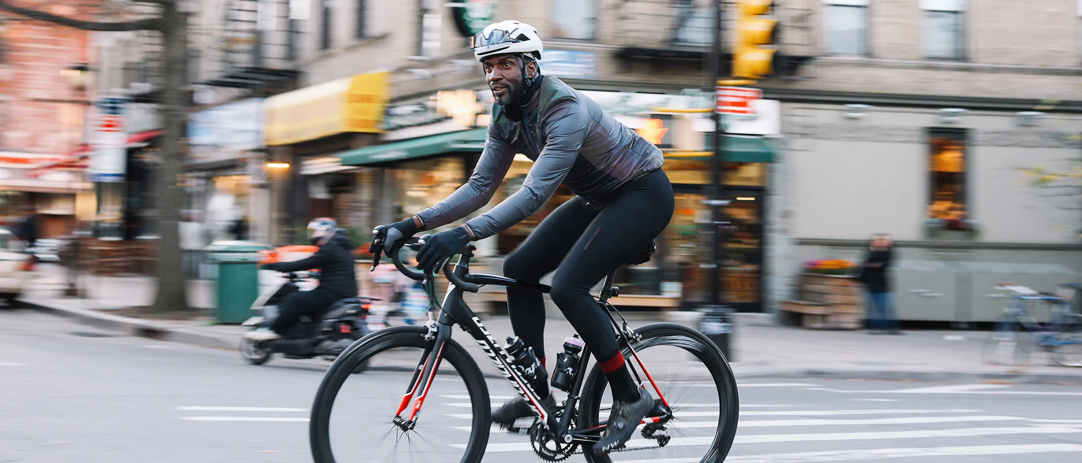 Man riding a road bicycle through a city street wearing cycling gear and a helmet.