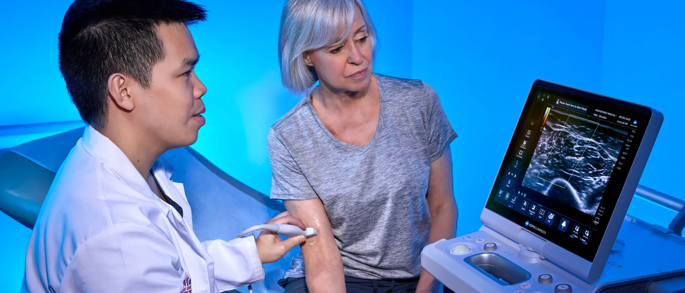 Doctor performing an ultrasound on a woman’s arm while showing her the scan results on a monitor.