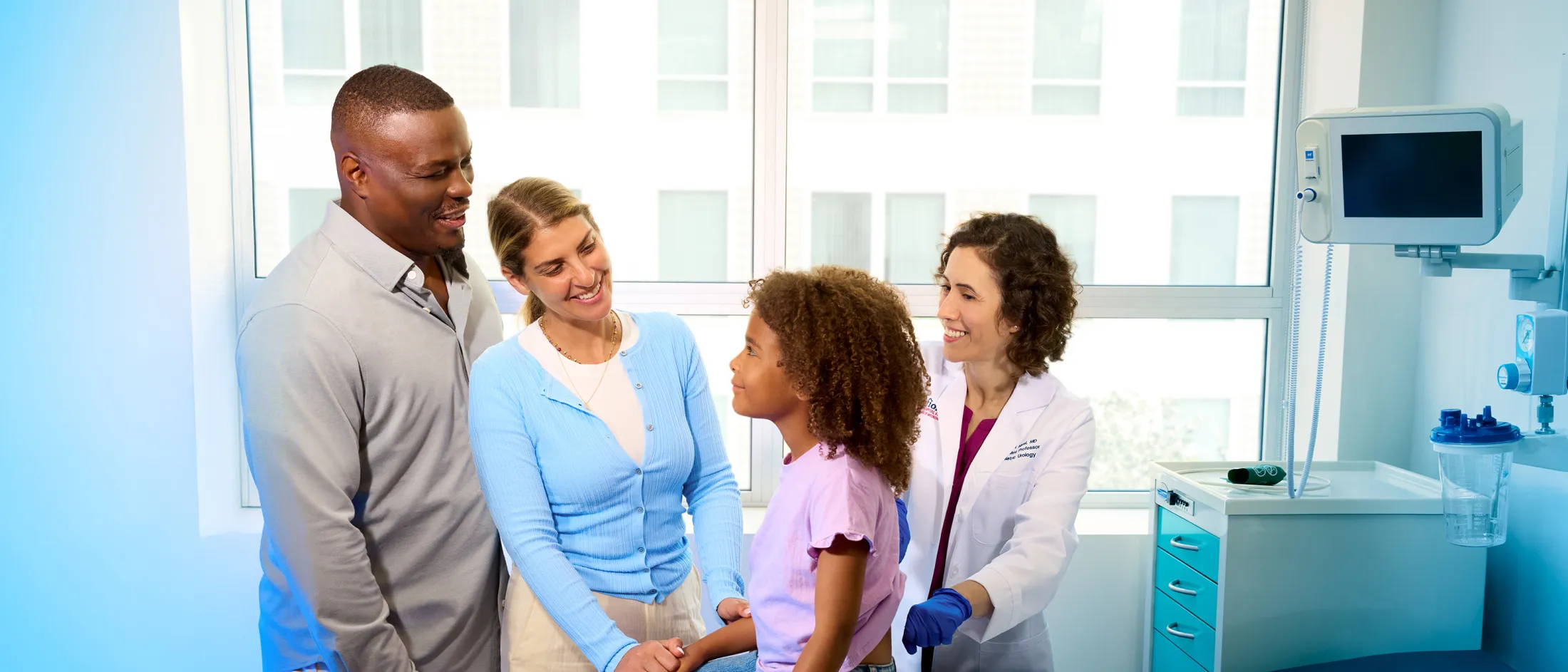 Pediatrician interacting with a young patient during a check-up, with parents present and smiling in a medical exam room.