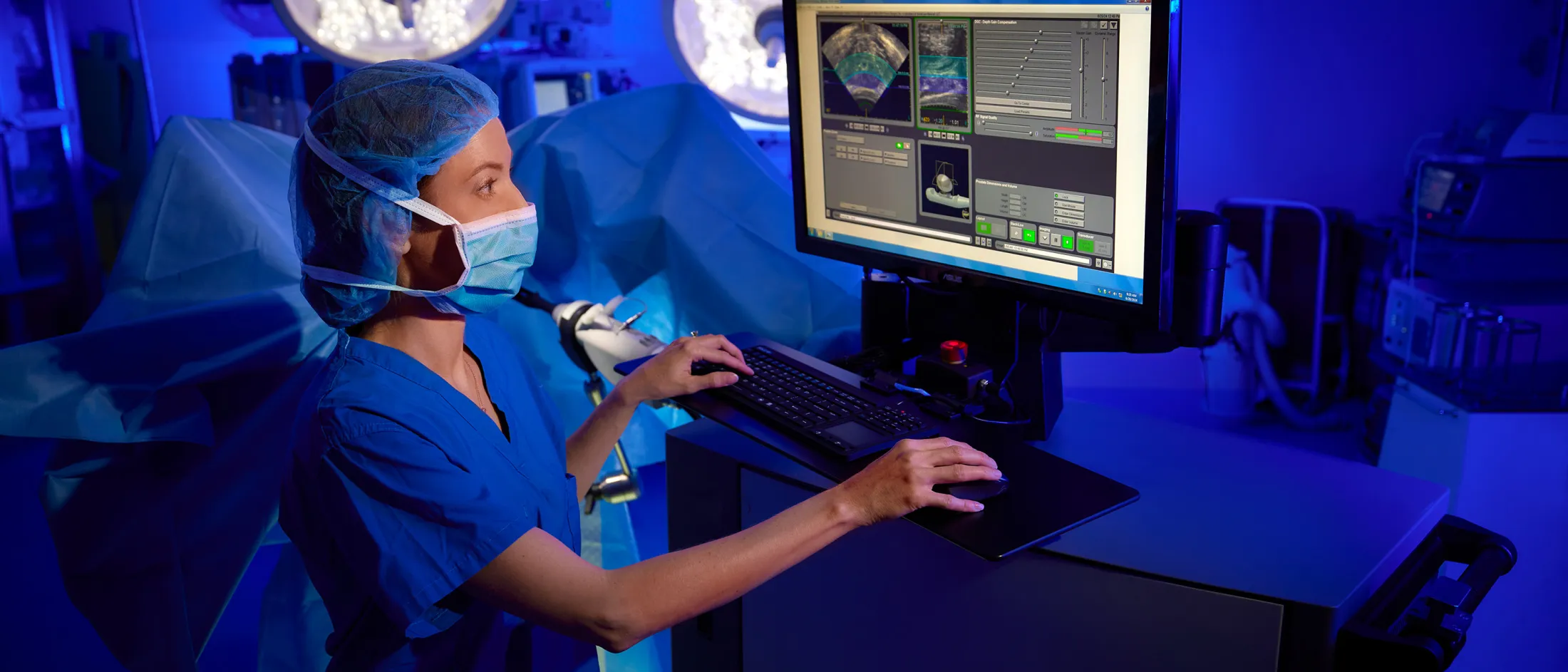Medical professional in blue scrubs operating imaging software on a computer in a surgical suite.