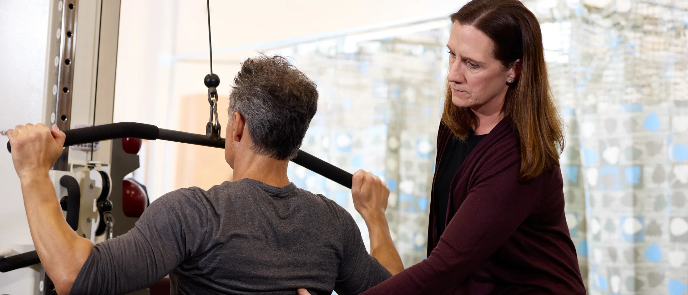 Therapist guiding a man using a lat pulldown machine during a rehabilitation session.