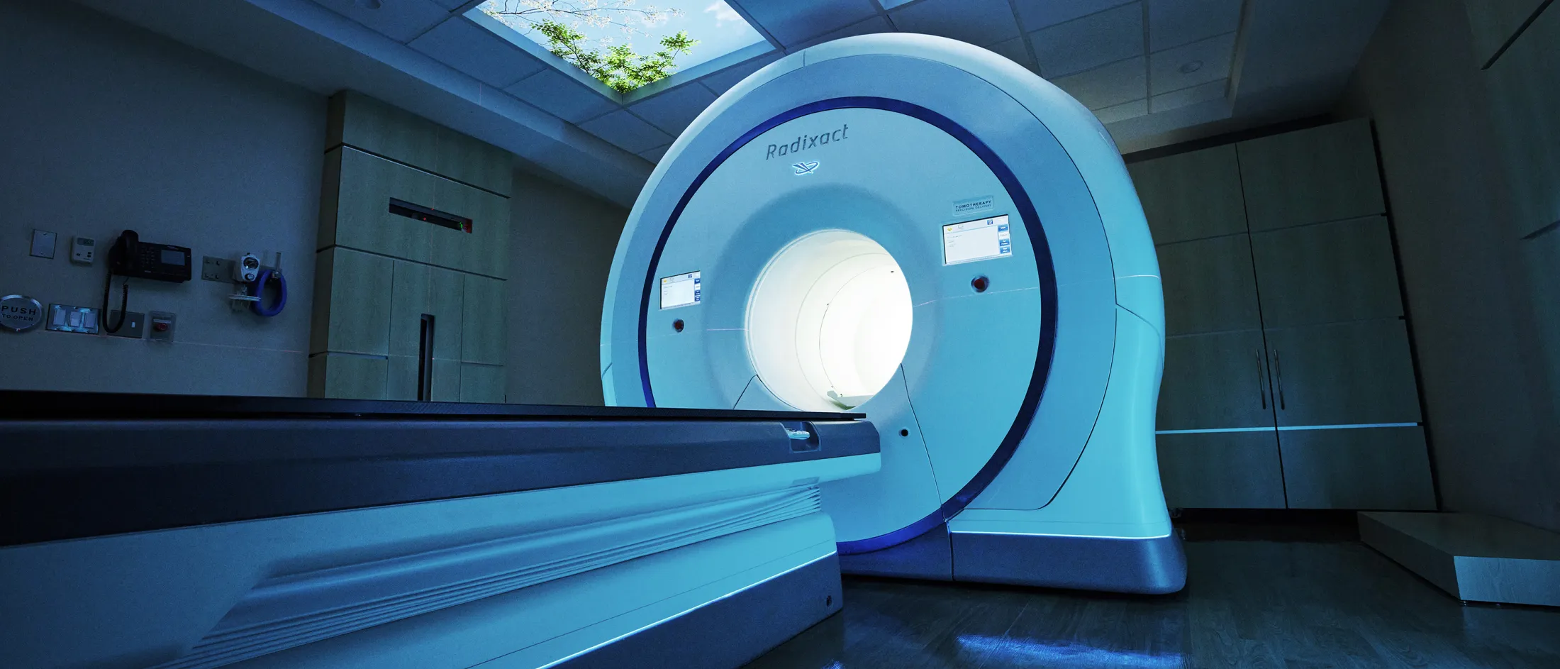 Modern Radixact radiotherapy machine in a softly lit treatment room with a nature-themed ceiling panel.