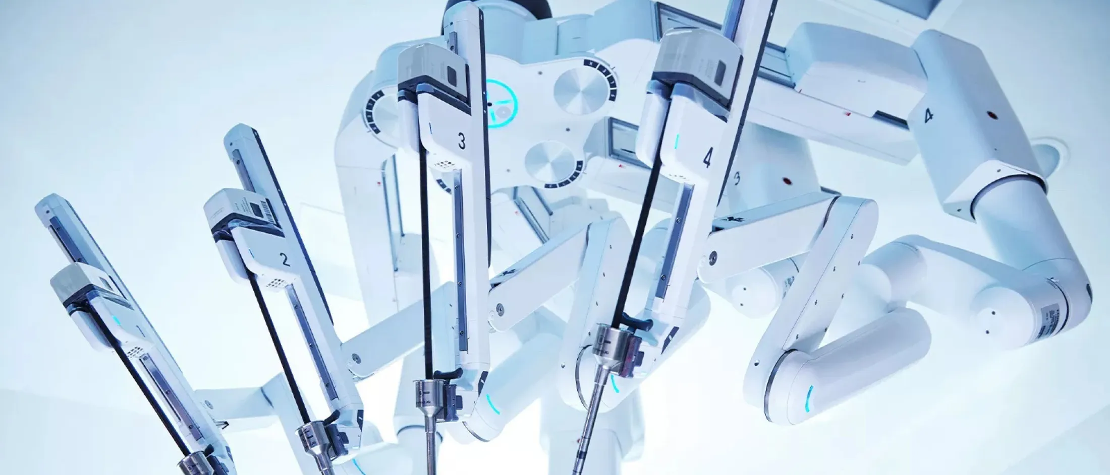Close-up of robotic surgical arms from a da Vinci surgical system, shown in a brightly lit operating room.