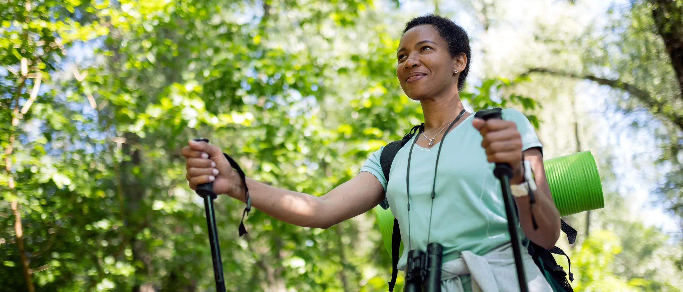 Smiling woman hiking through a green forest with walking poles and a backpack, enjoying nature