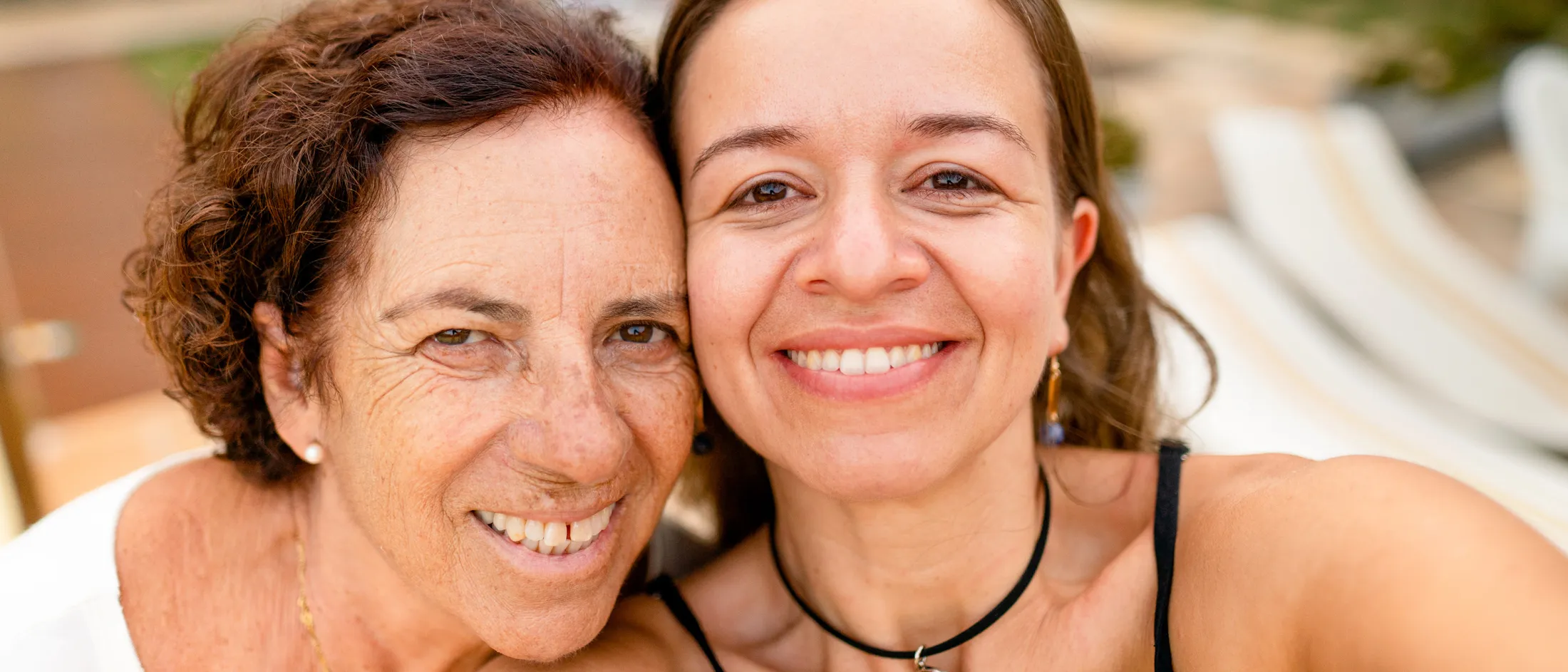 Older woman and younger woman smiling closely for a cheerful outdoor selfie.