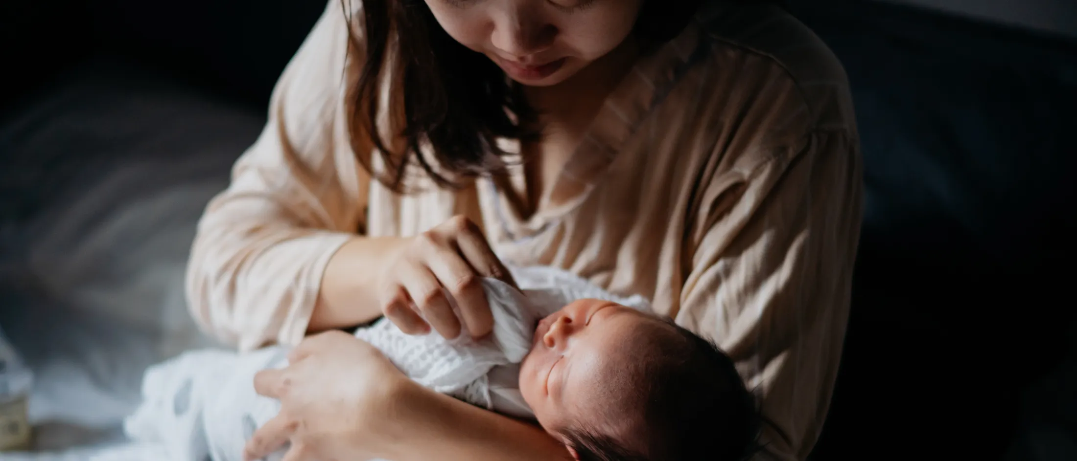 Mother holding her newborn baby in bed, gently touching the baby’s face in soft, natural light.