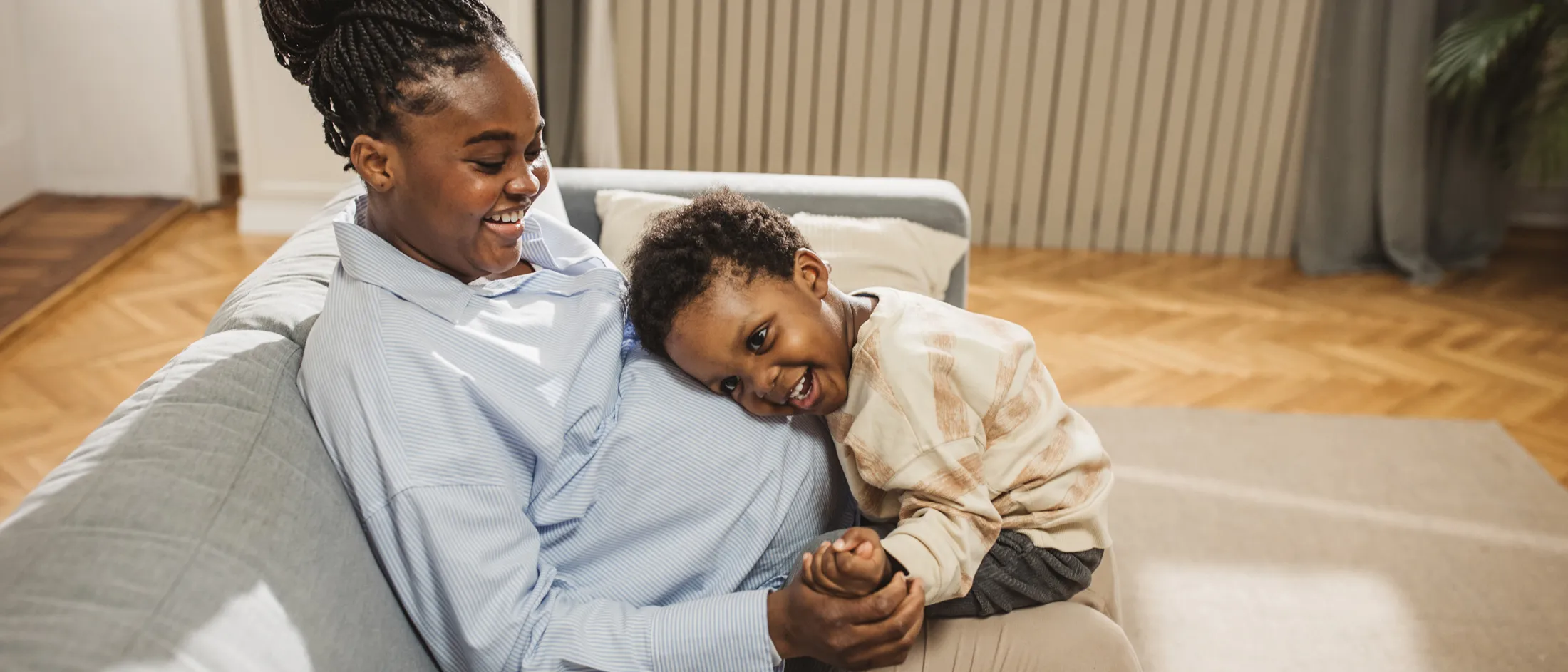 Smiling pregnant woman sitting on a couch with her young child resting their head on her belly.