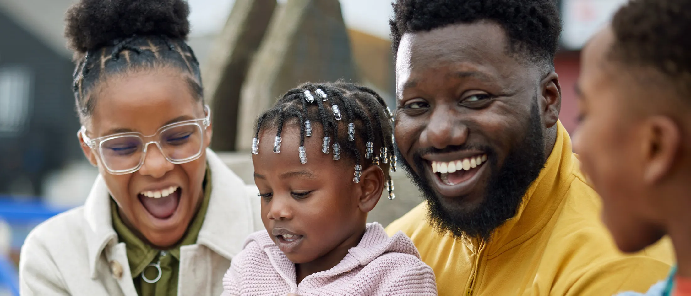 Family of four enjoying a joyful moment together outdoors, with everyone smiling and laughing.
