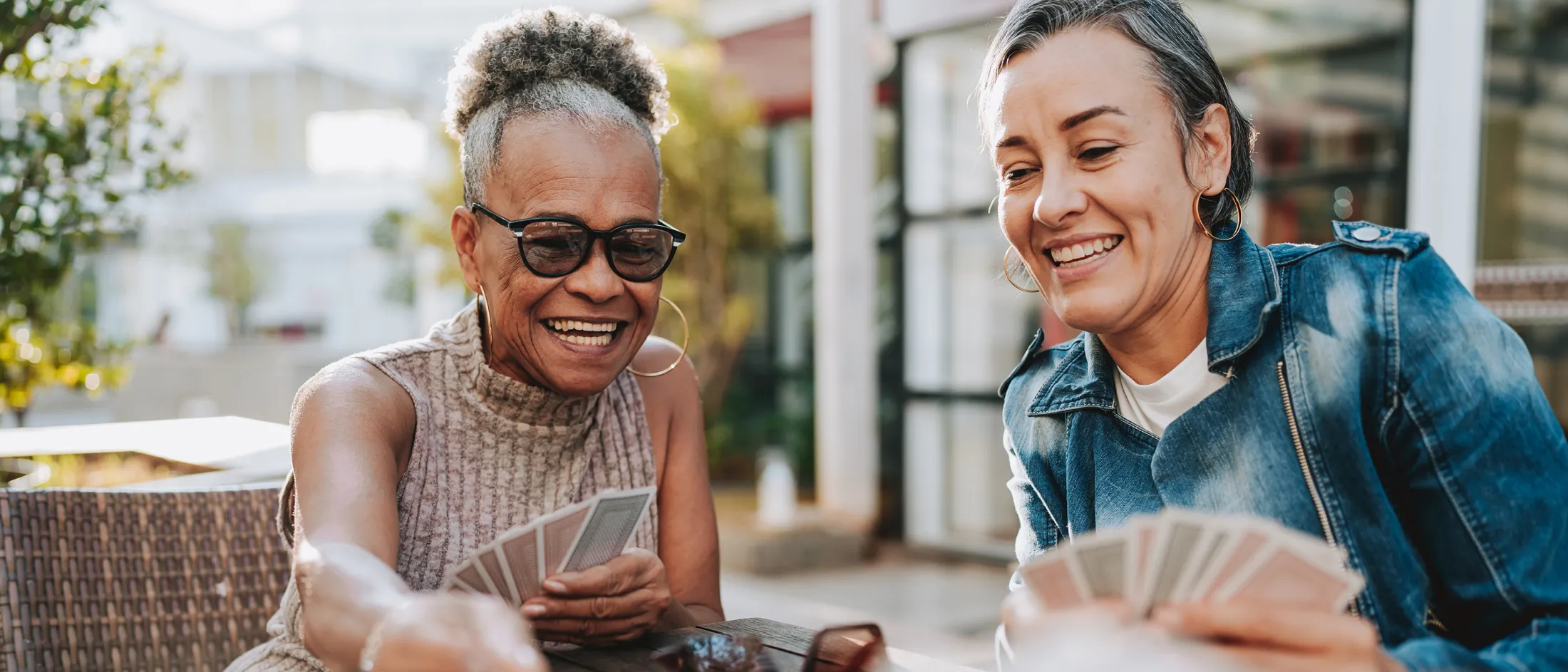 Two women playing cards at an outdoor table, smiling and enjoying a sunny day together.