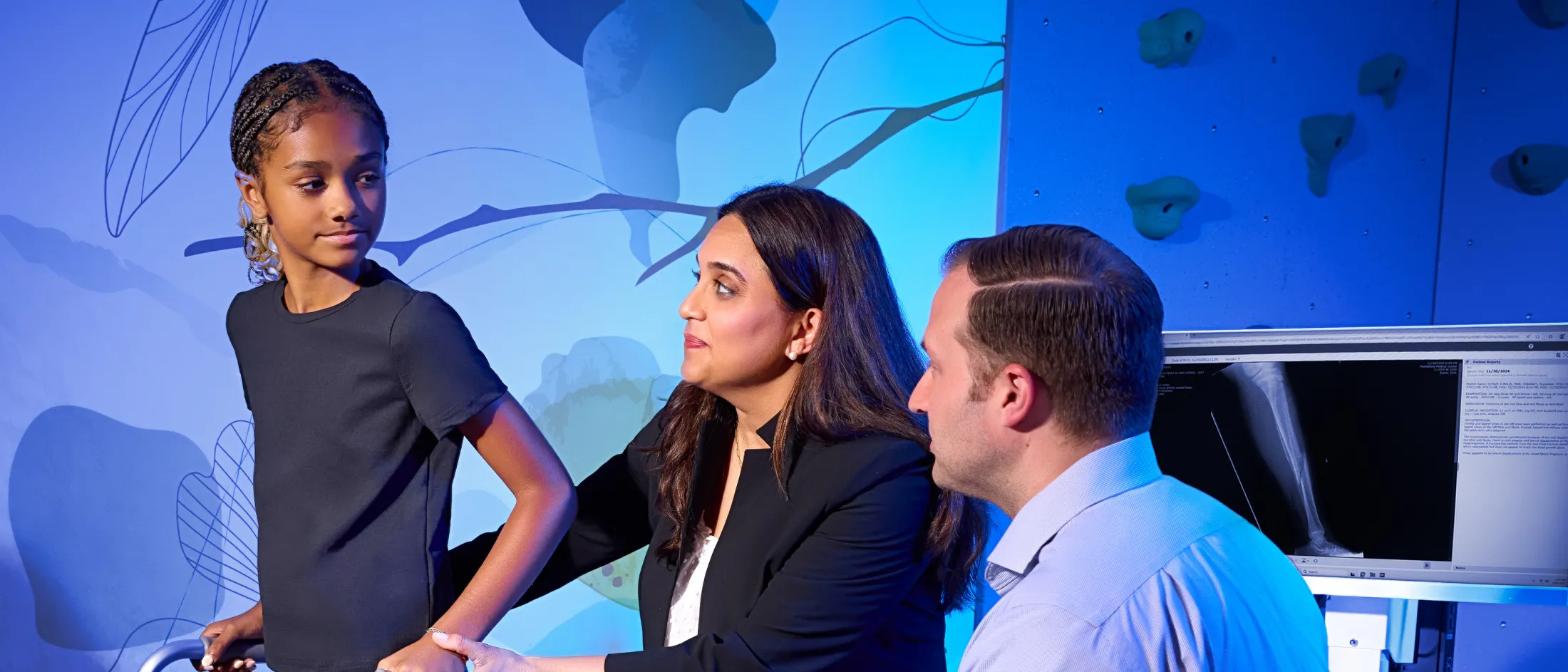 Young girl using a walker as two doctors observe and support her in a pediatric rehabilitation setting.