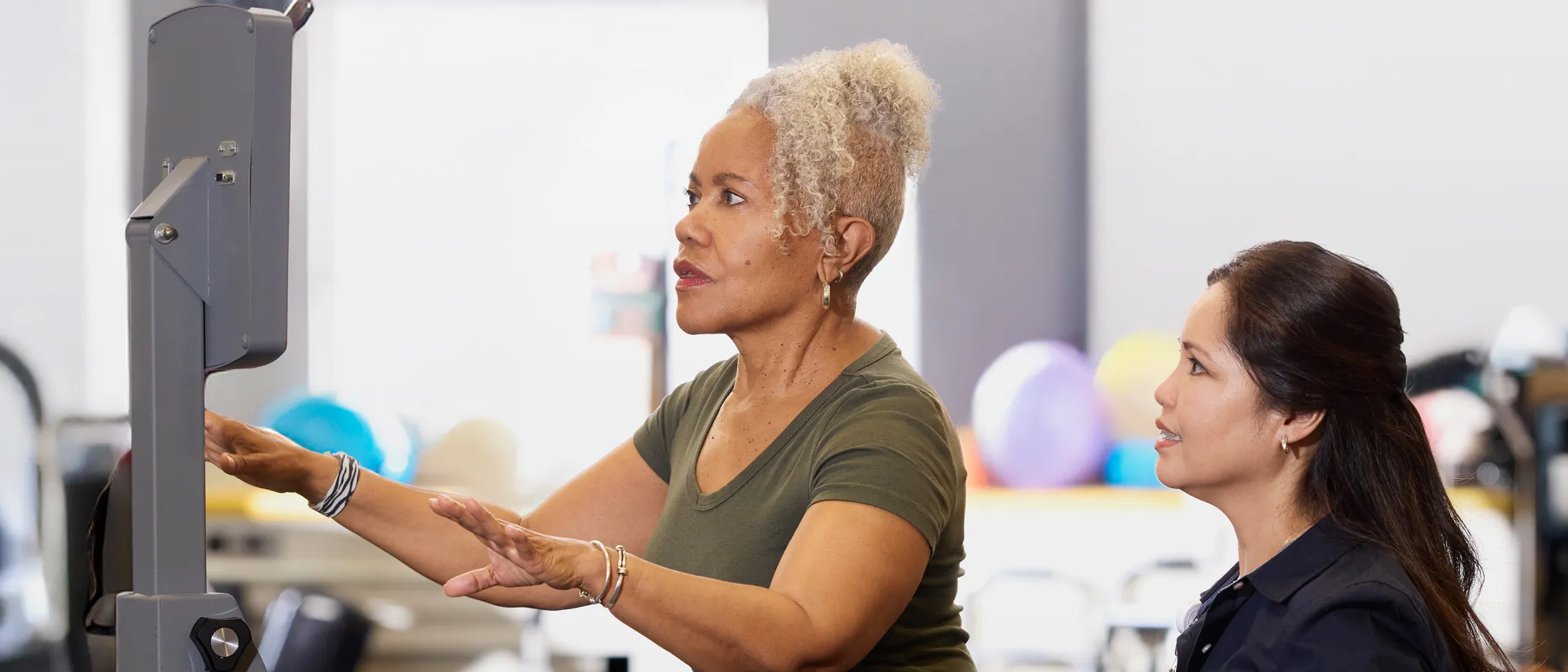 Therapist guiding an older woman using a balance machine during a vestibular rehab session.