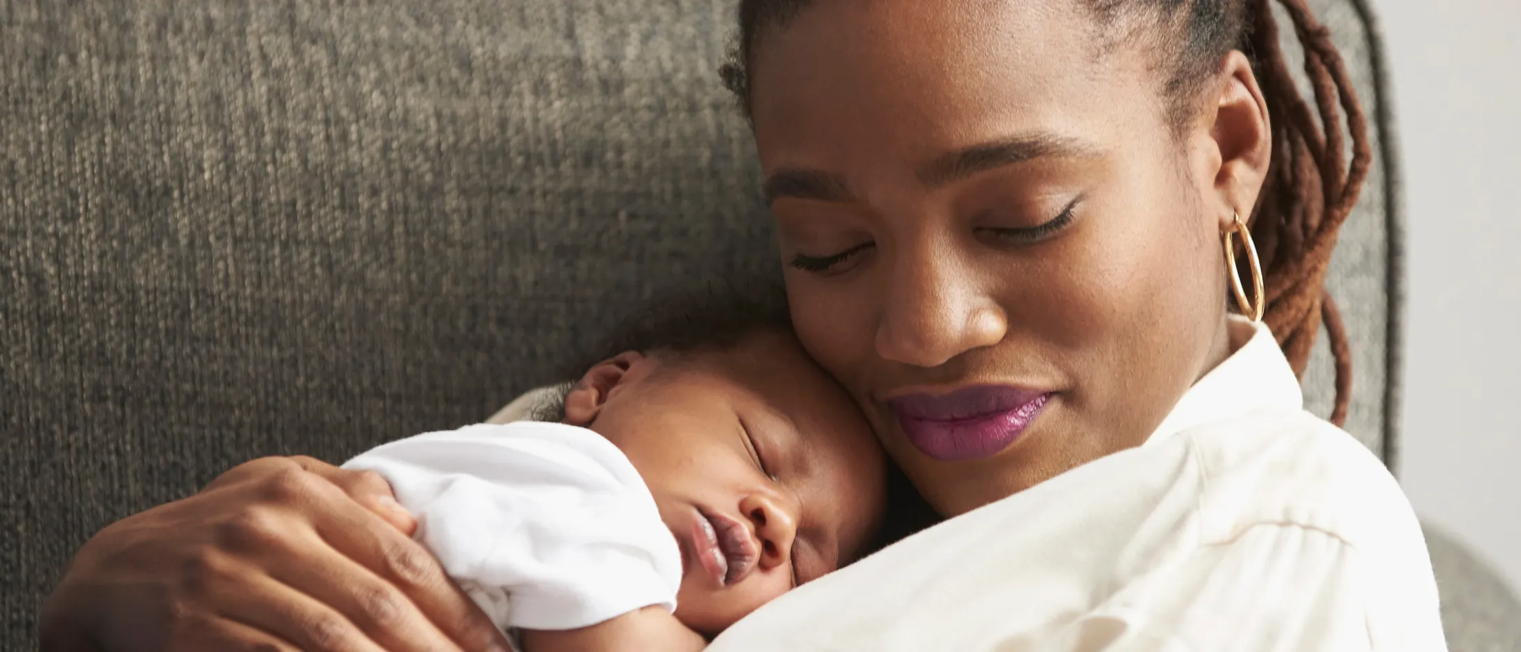 Mother peacefully holding her newborn baby on a couch.