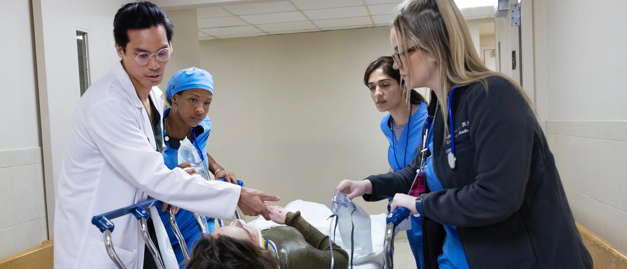 Emergency department team rushes a patient on a stretcher through a hospital hallway, actively coordinating care.