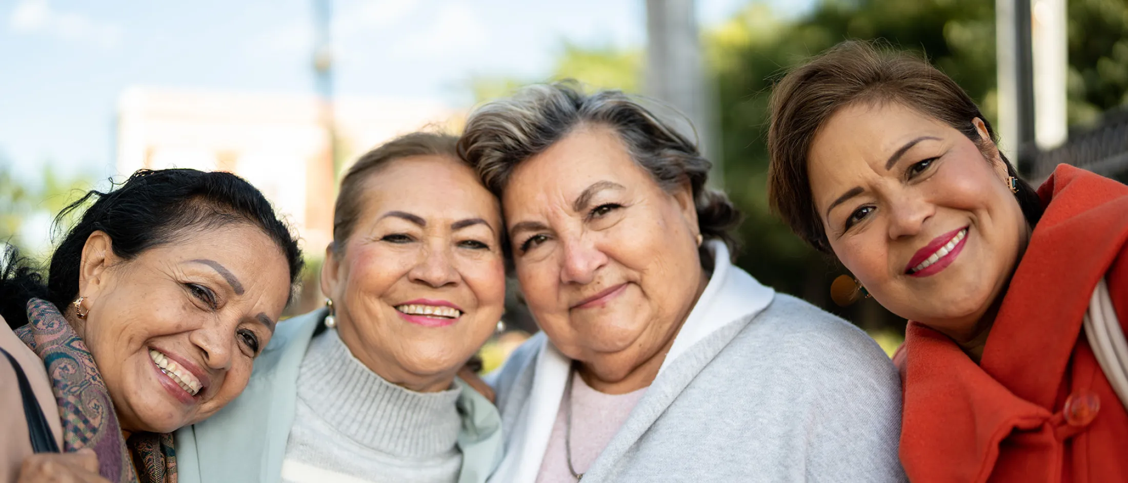 Four older women smiling closely together outdoors on a sunny day