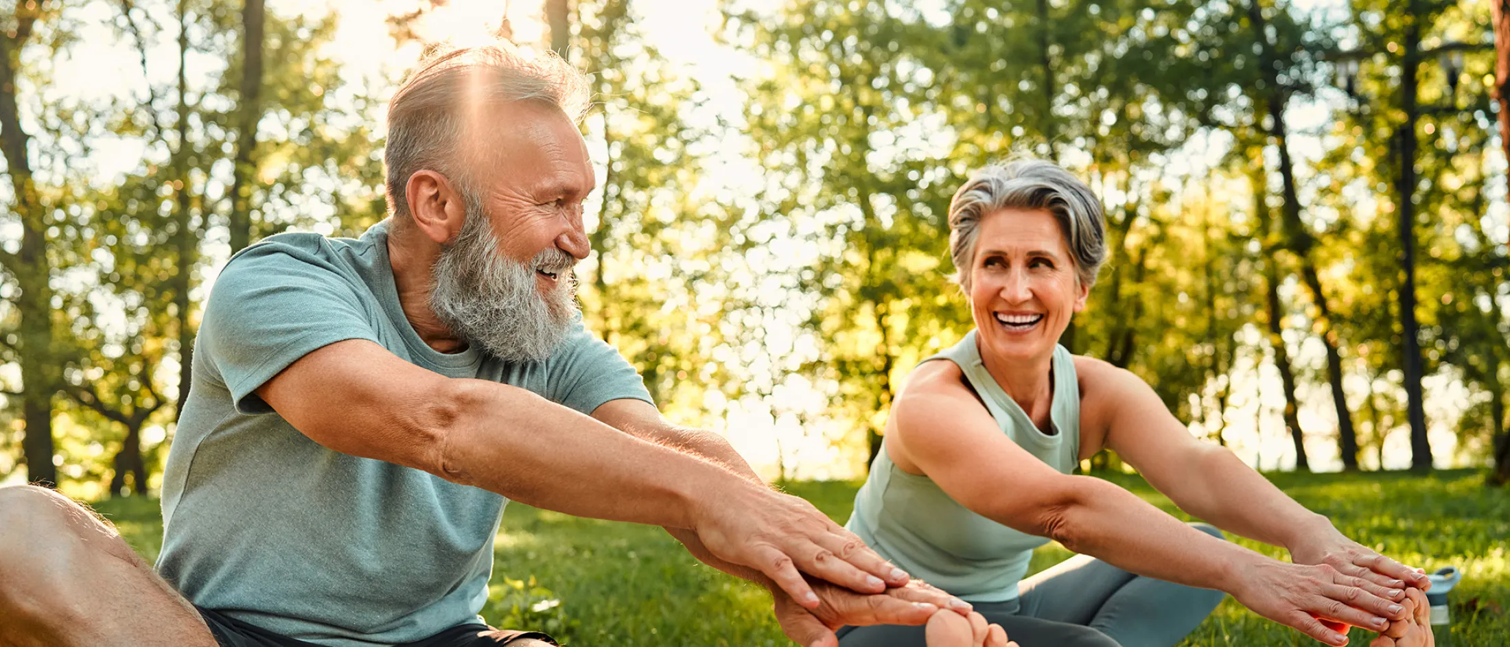 Senior couple stretching outdoors together on a sunny day.