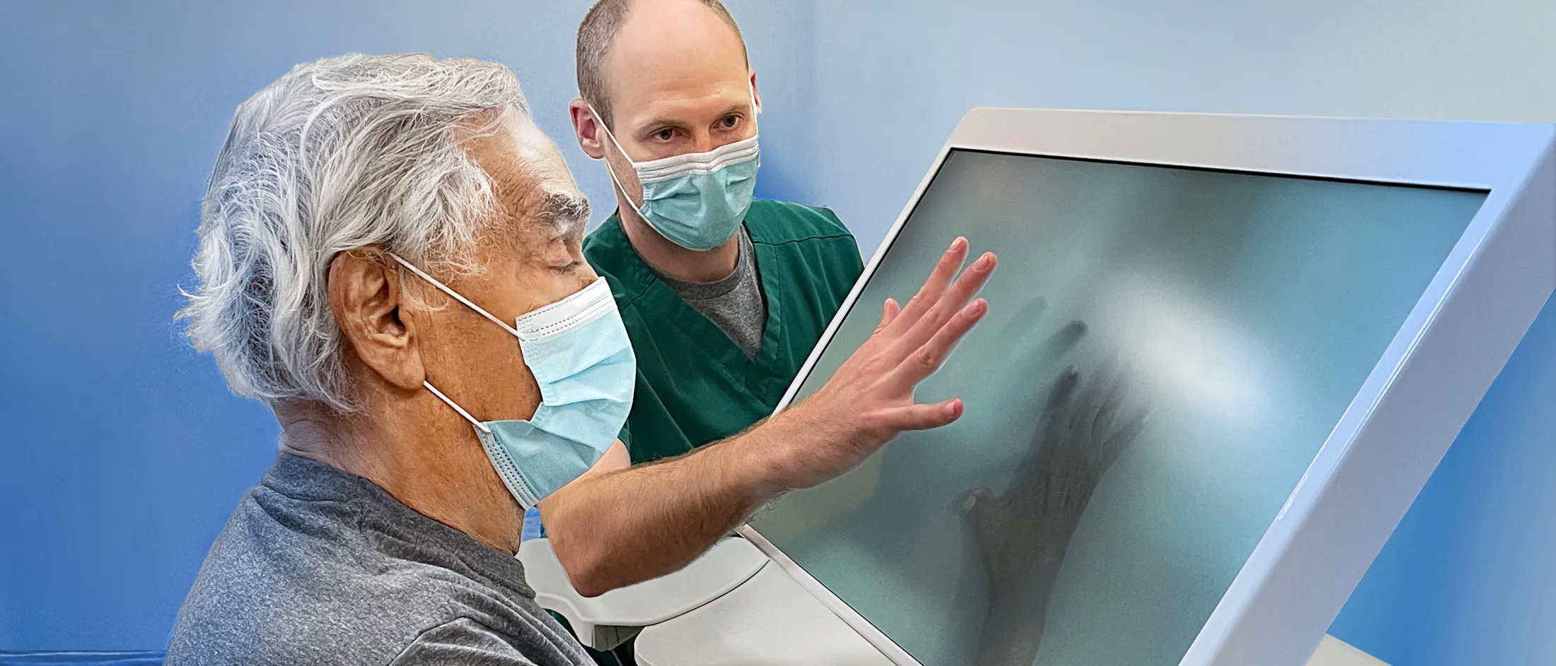Doctor assisting an elderly patient with a touchscreen medical display.
