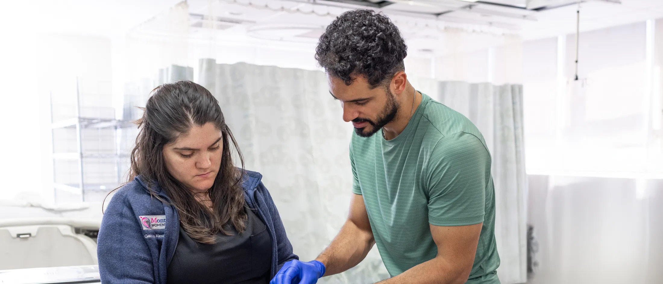 Two people in a clinical simulation center work together on a medical training device, wearing gloves and focused on a hands-on procedure.