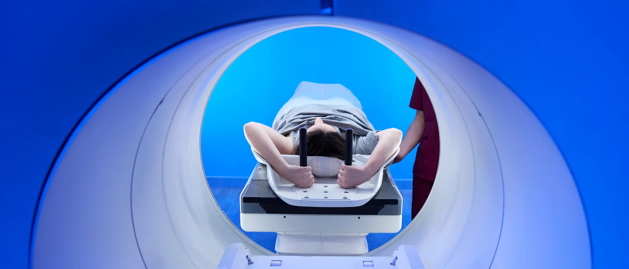 Patient lies on a table entering an MRI scanner illuminated with blue light