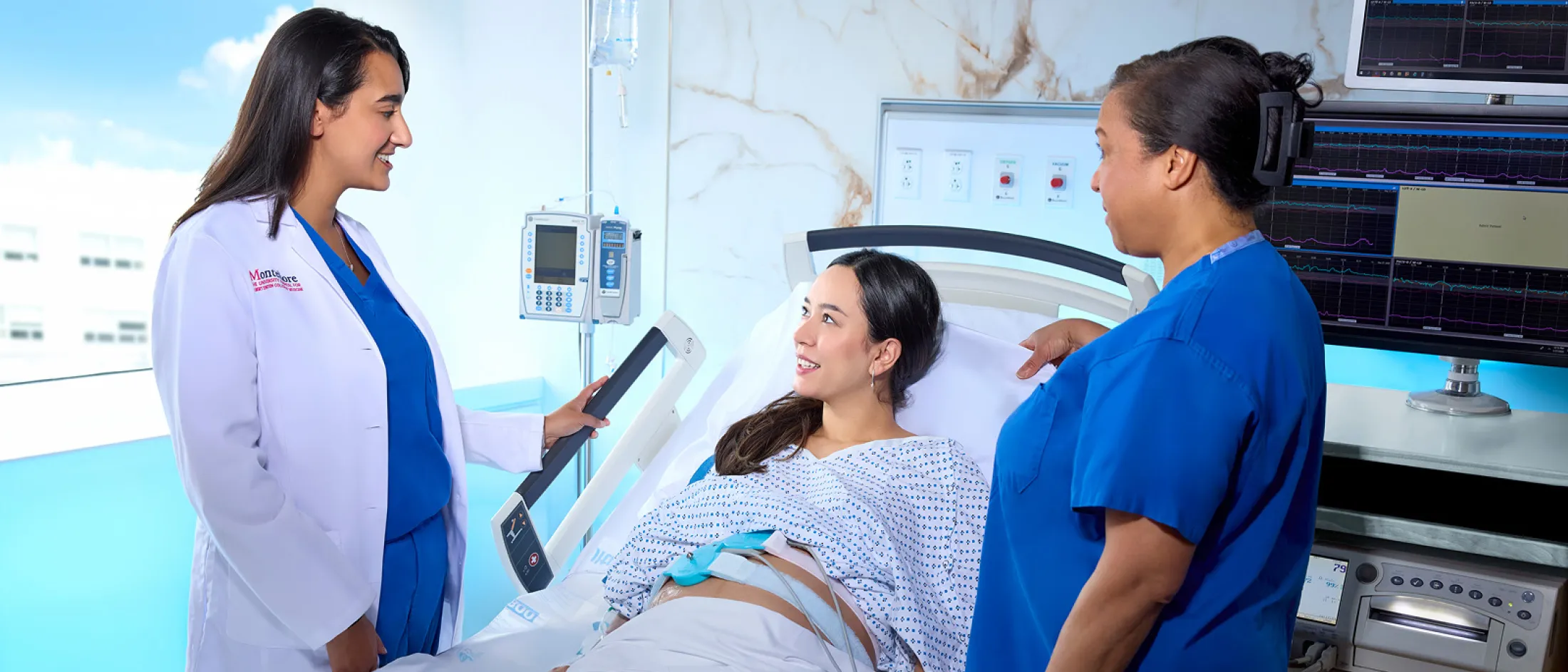 A pregnant patient lies in a hospital bed while a doctor in a white coat and a nurse in blue scrubs provide care and support in a modern labor and delivery room.