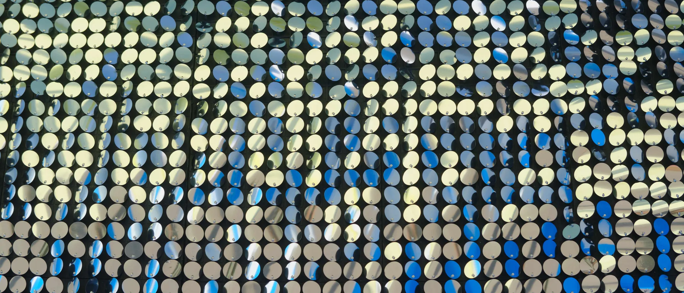 Image of small round mirrors arranged in rows and columns on a black background that sparkle and glitter.