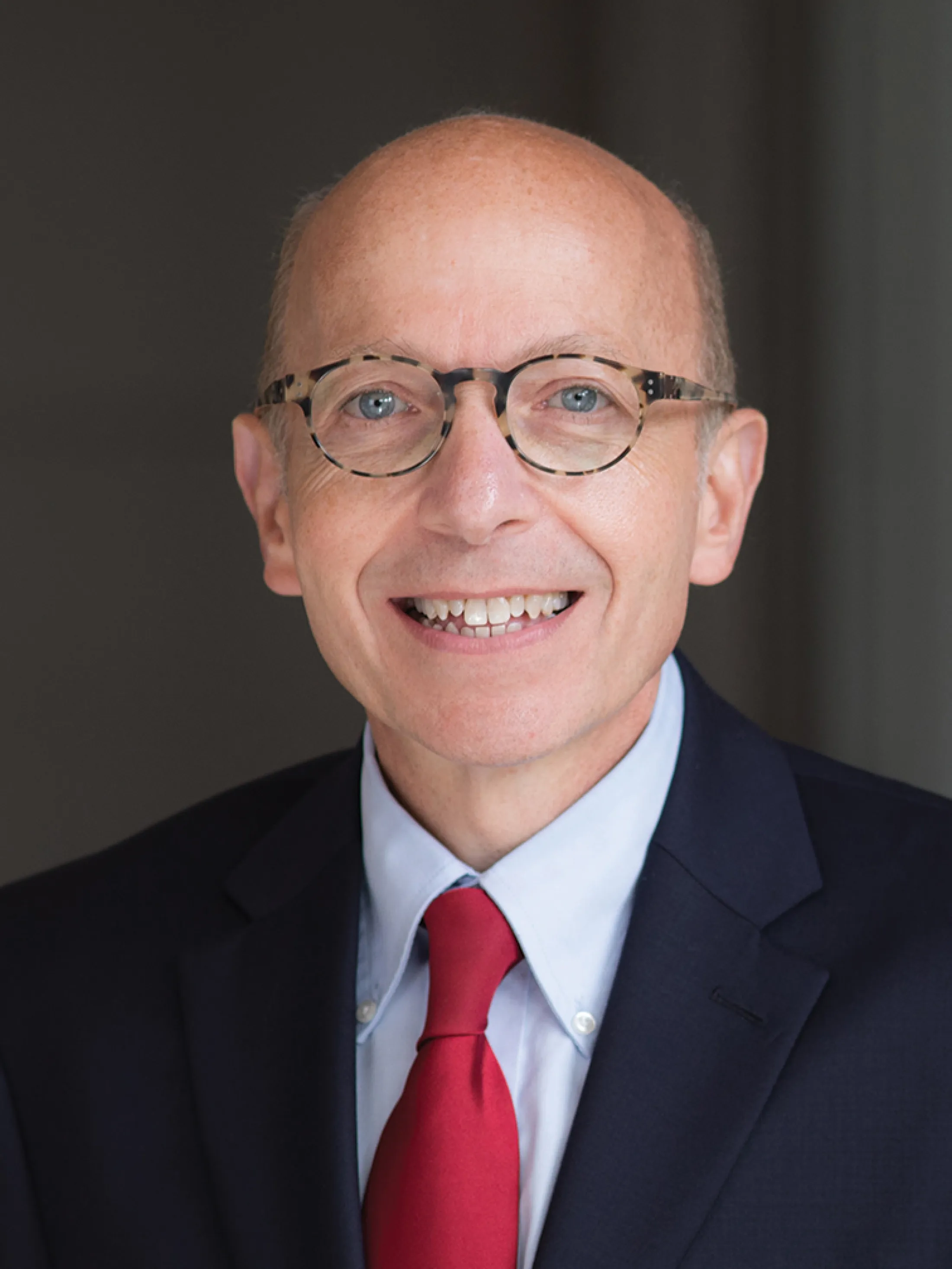 Portrait of Dr. Jonathan Alpert wearing glasses, a dark suit, light blue shirt, and red tie, smiling at the camera.