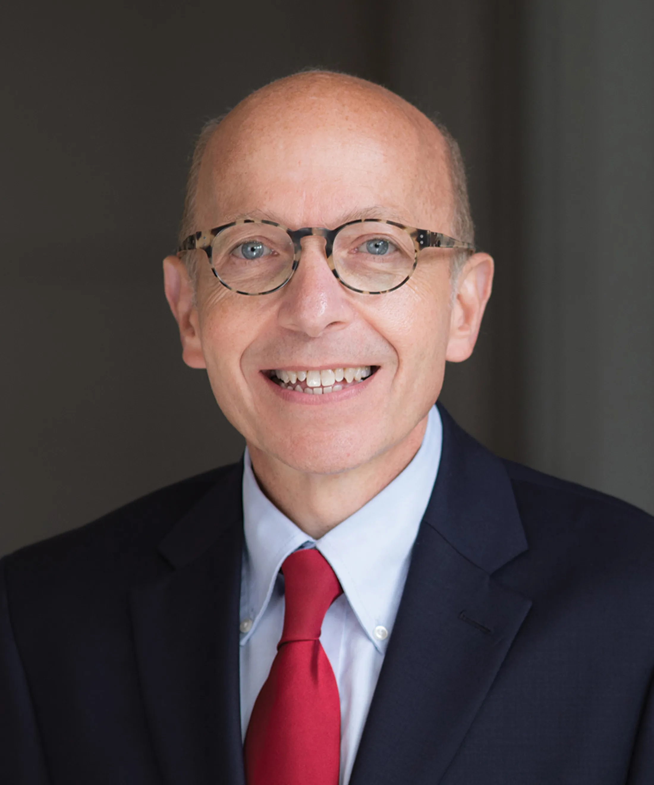 Portrait of Dr. Jonathan Alpert wearing glasses, a dark suit, light blue shirt, and red tie, smiling at the camera.