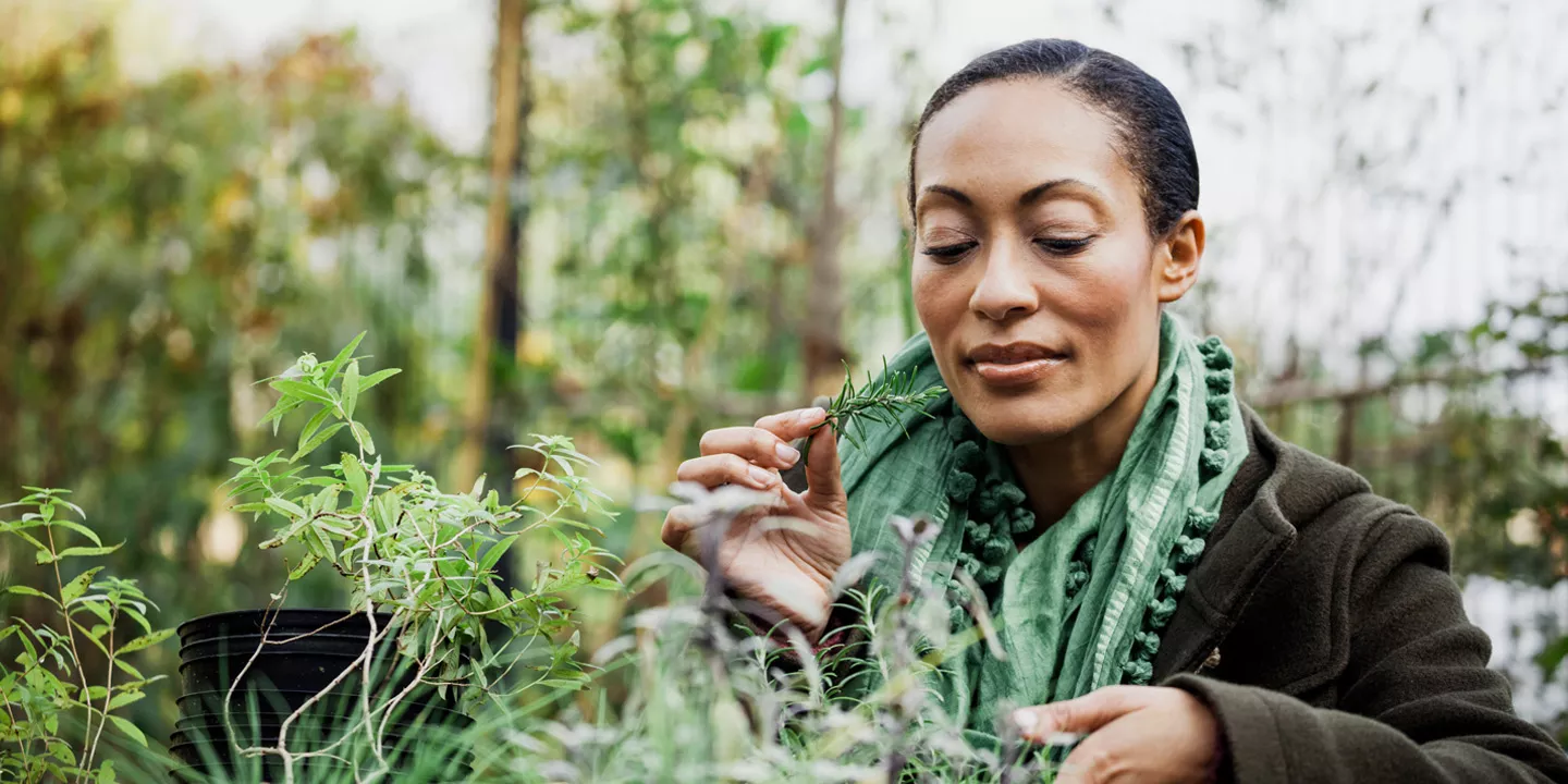Woman brings an herb to her face in a garden.