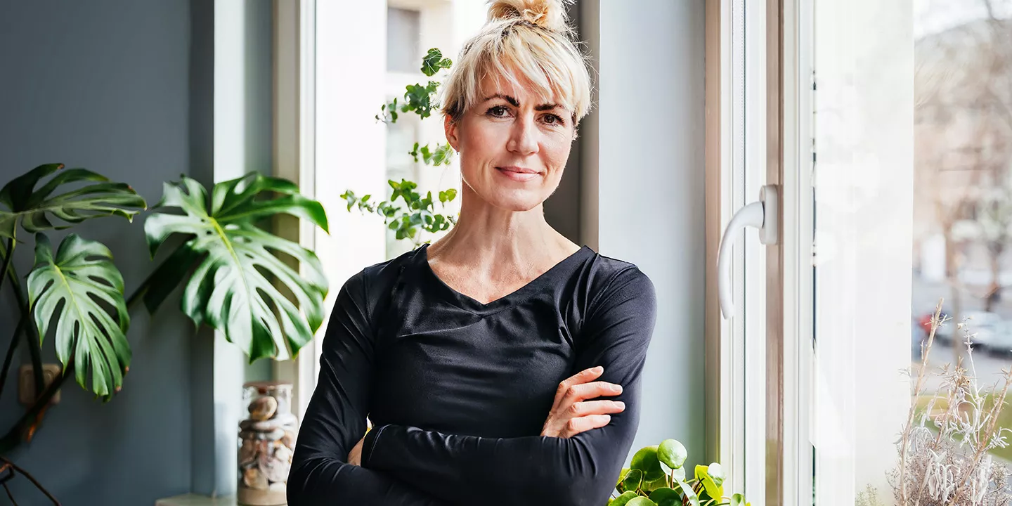Woman with arms crossed standing next to window.