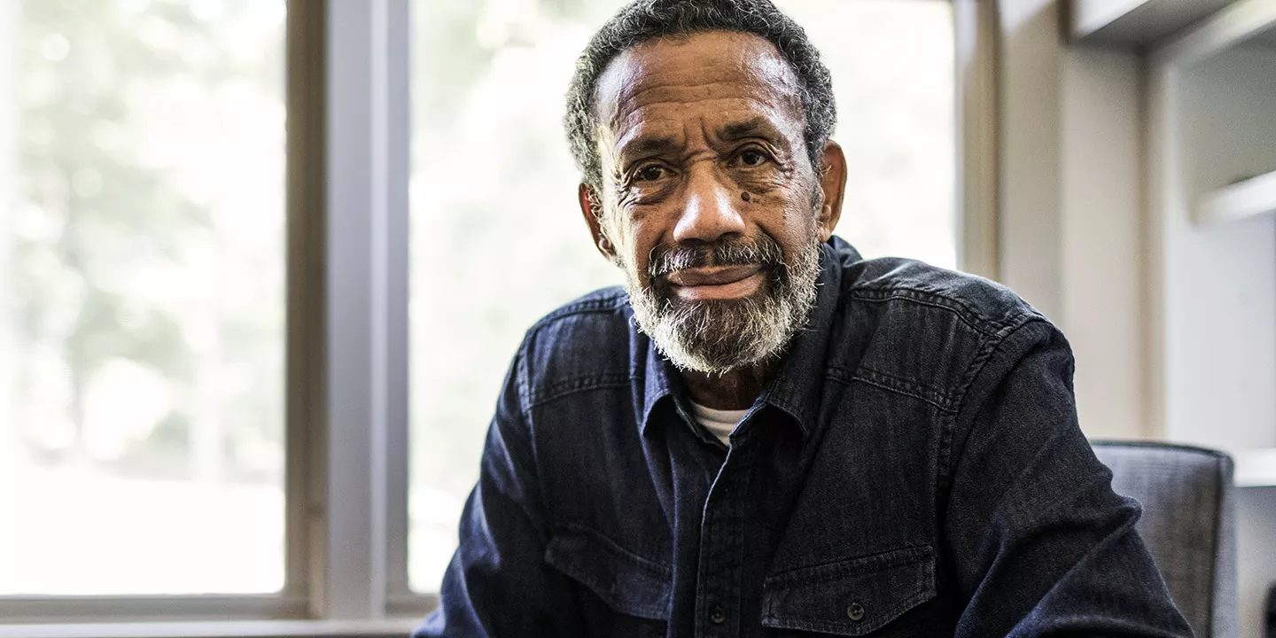 A man framed by sunny windows smiles toward the camera.