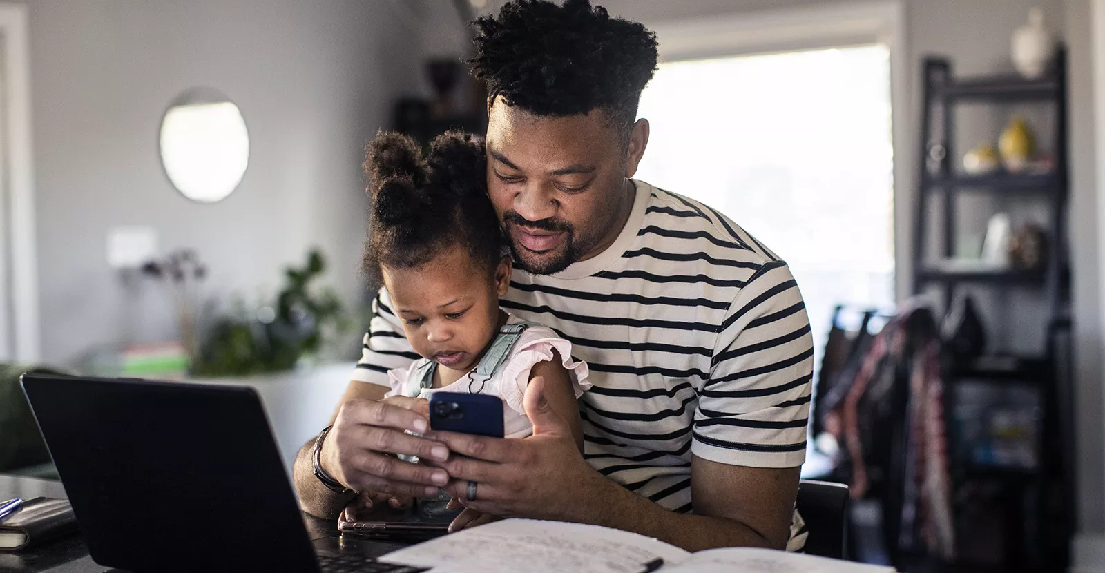 Father using mobile device with his daughter sitting on his lap.