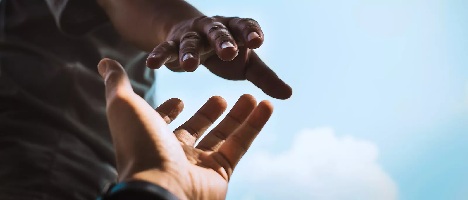 Two hands extending toward one another against blue sky.