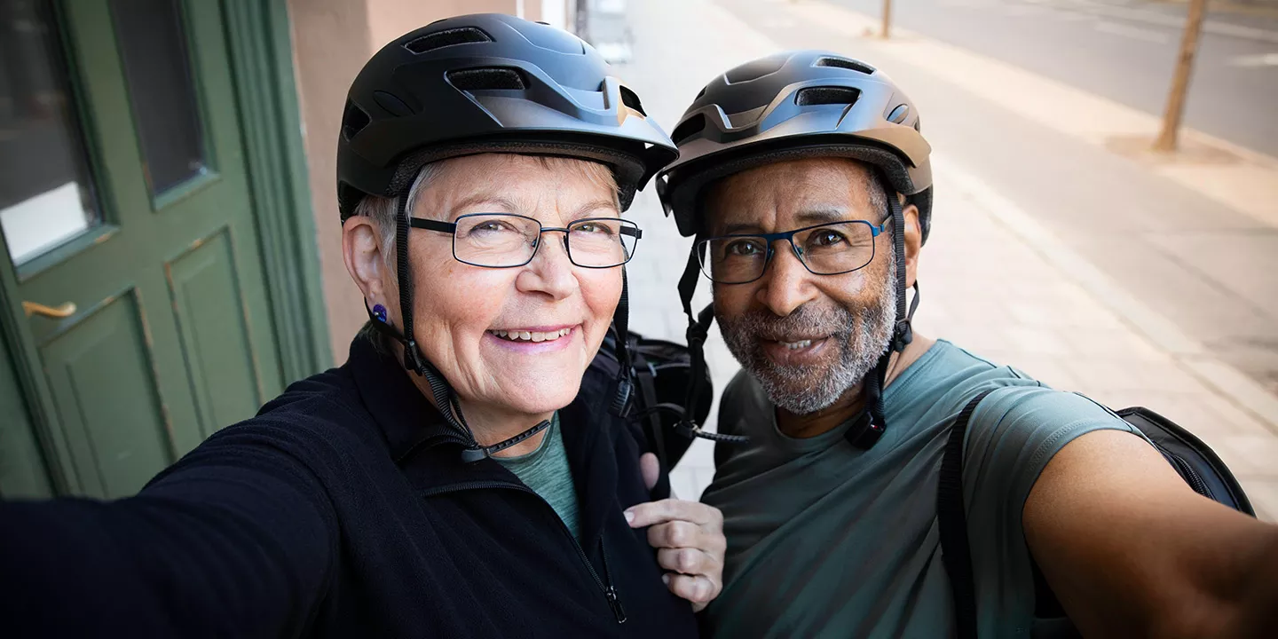 Man and a woman wearing bike helmets smiling at camera.