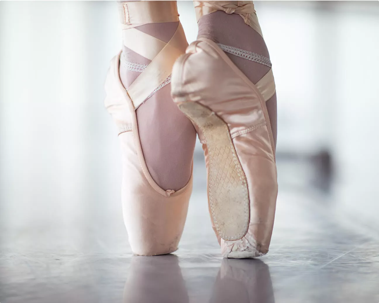 A closeup of a ballerina's feet in light pink shoes, up on toes