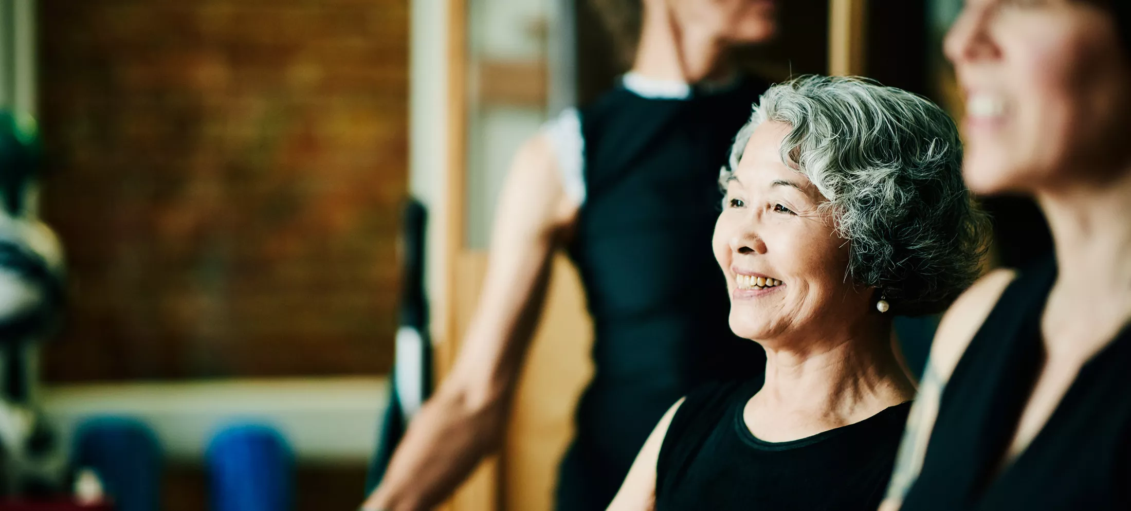 Smiling mature woman hanging out with friends in pilates studio while resting between exercises