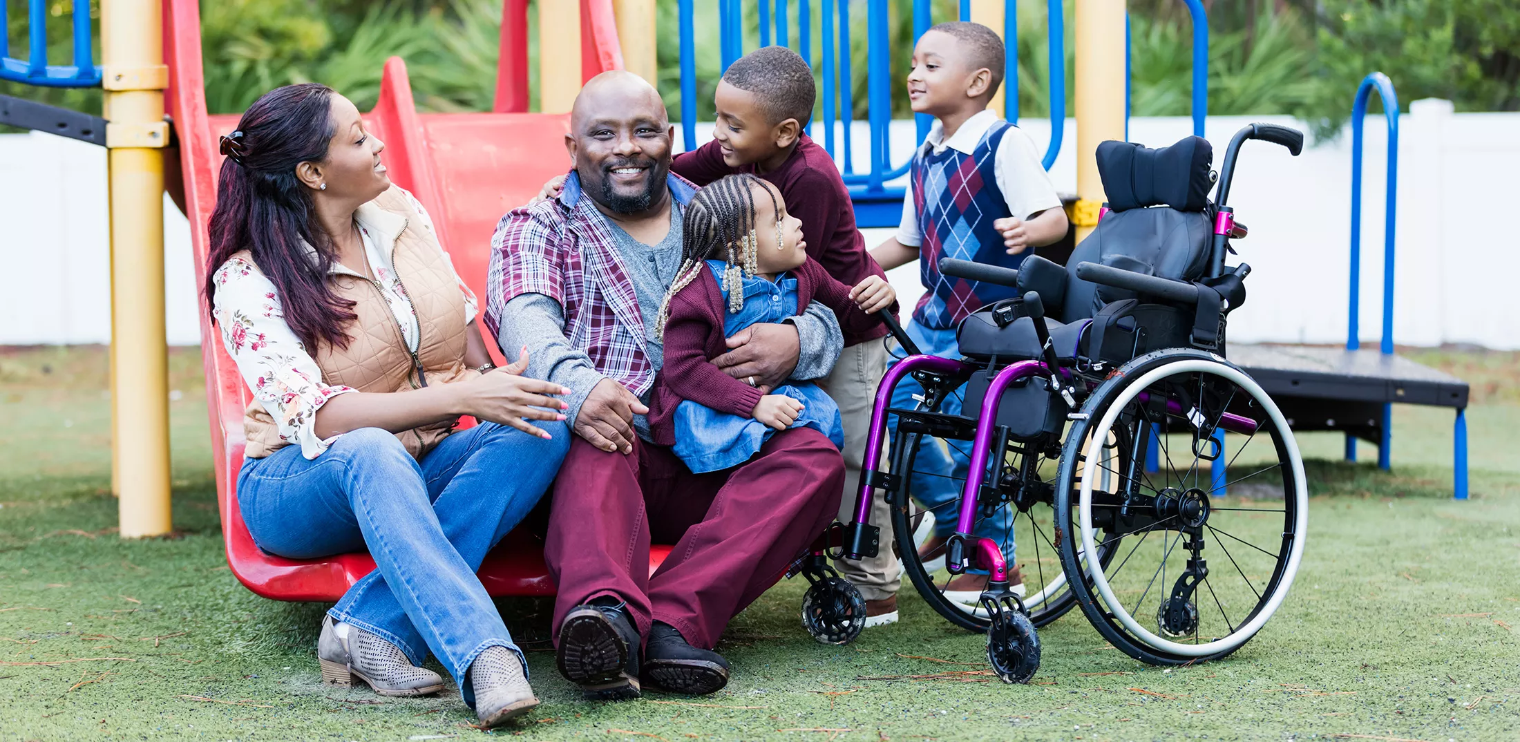 A happy African-American family with three young children sitting together on a playground. 