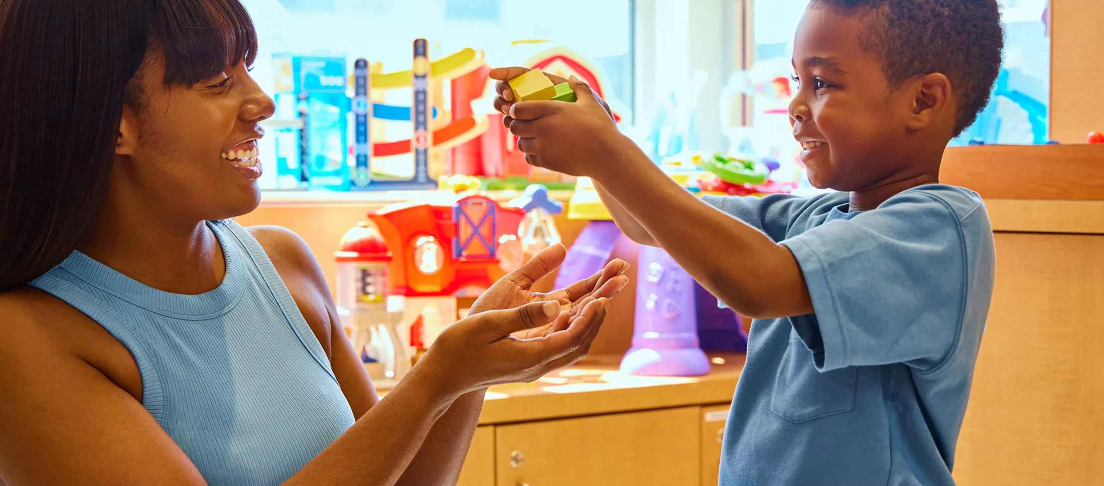 A young boy playing with toys in a playroom with his mother