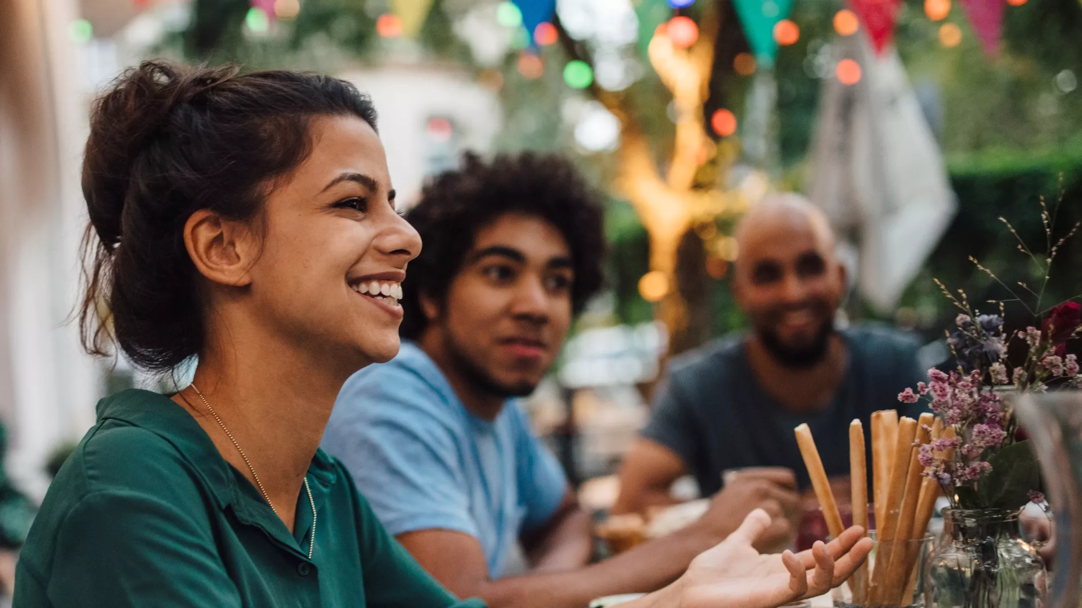 A siming young woman gesturing while sitting with friends at a table during a dinner party