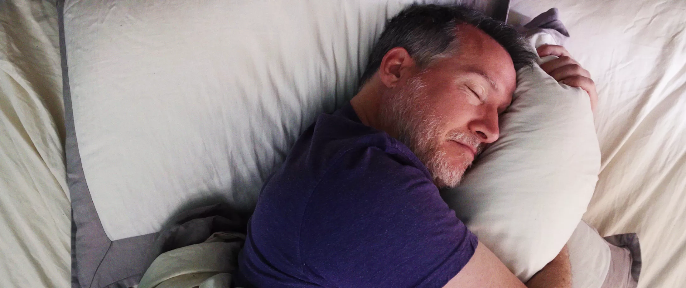 Man in bed hugging pillow while sleeping