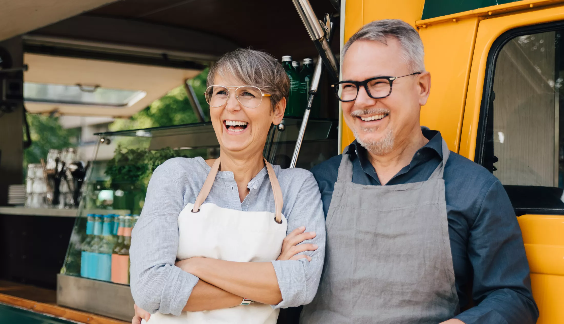 A happy couple looking away while standing against their food truck.