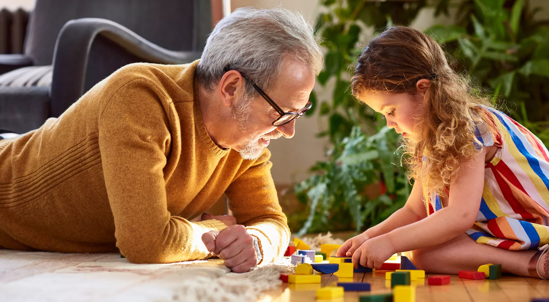 Granddaughter playing with wooden block and granddad watching