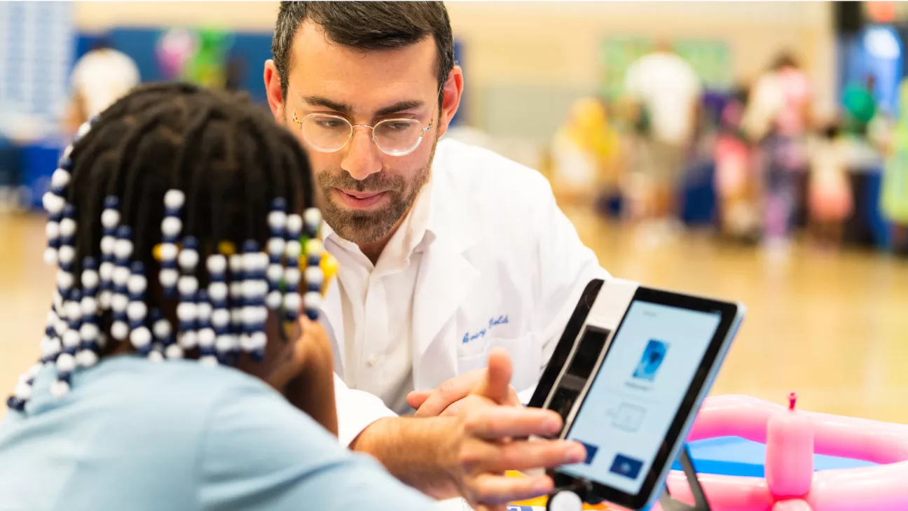 A physician guiding a young adult on a tablet at a community event
